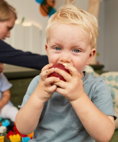 Krippenkind beißt in einen roten Apfel in der Kita kinderzimmer Hamburg