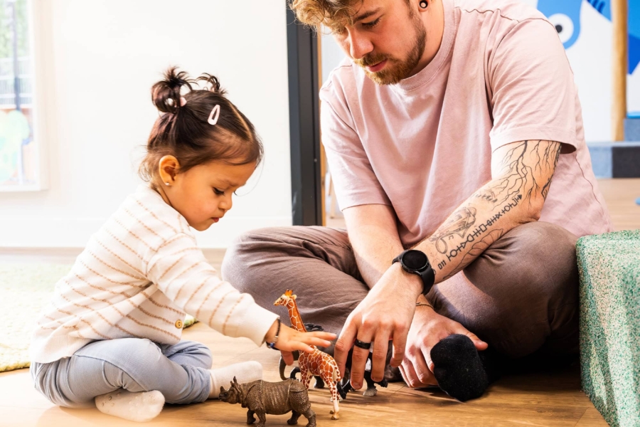Ein Erzieher spielt zusammen mit einem Kind mit Zoofiguren in der Kita kinderzimmer Hamburg