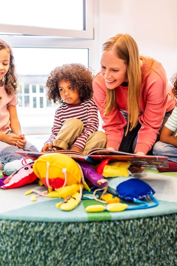 Eine Pädagogin liest einer Gruppe ein Buch vor in der Kita kinderzimmer Hamburg