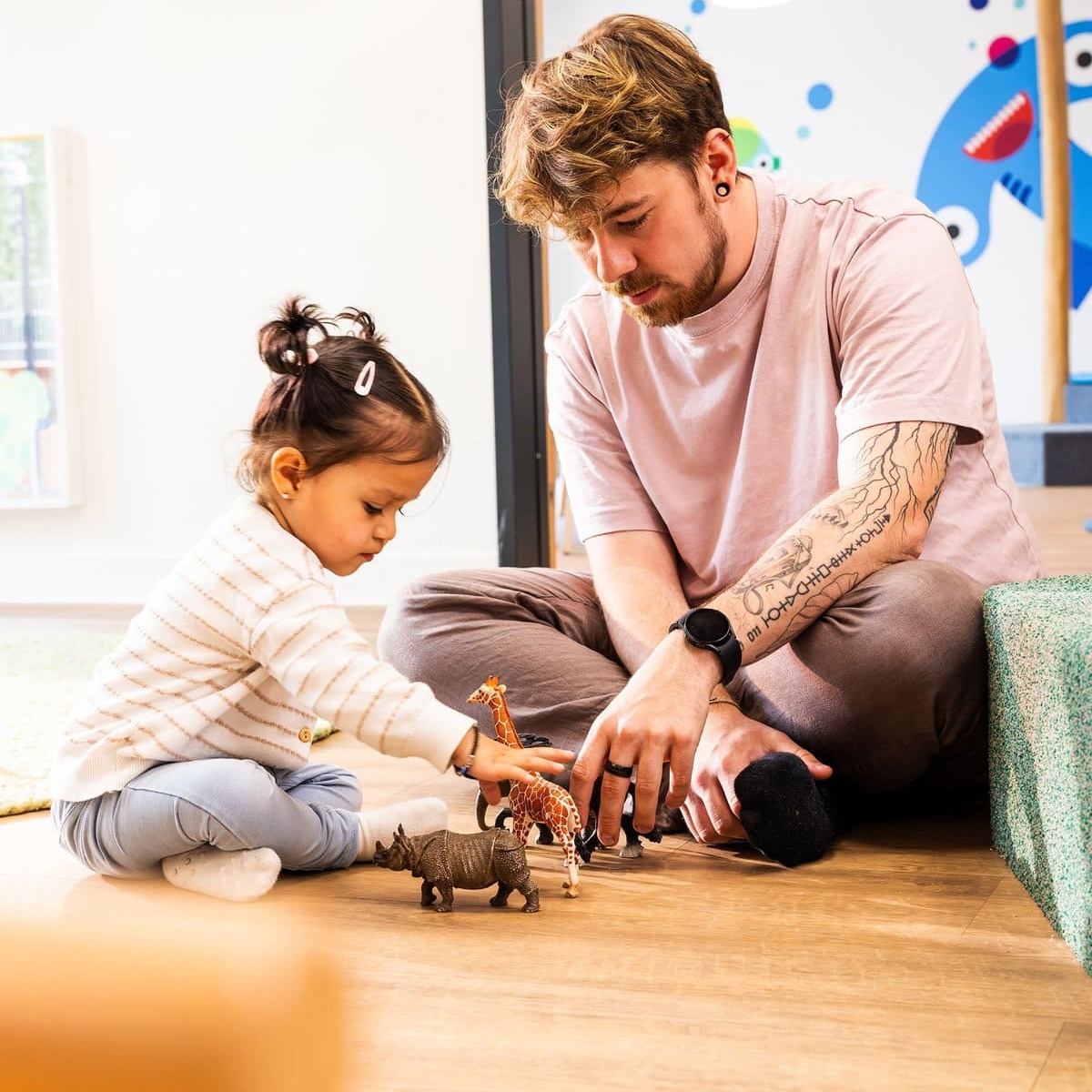 Pädagoge spielt, sitzend auf dem Boden, mit Kleinkind und Spielzeugtieren