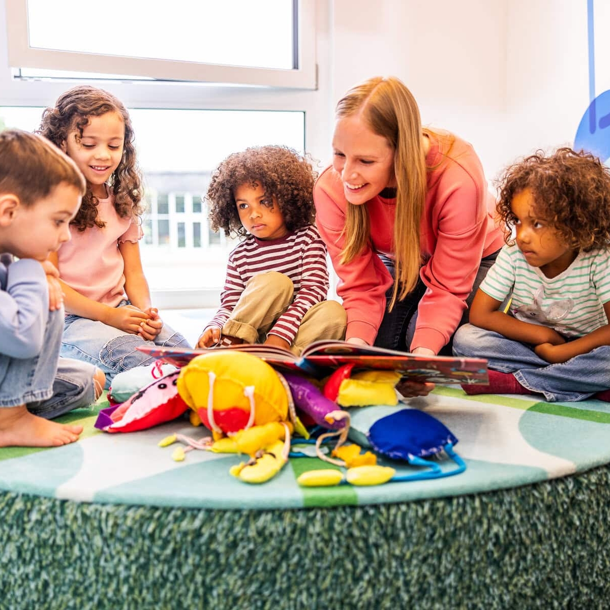 Eine Erzieherin liest mit einer Gruppe Kinder in einem Buch in der Kita kinderzimmer Hamburg