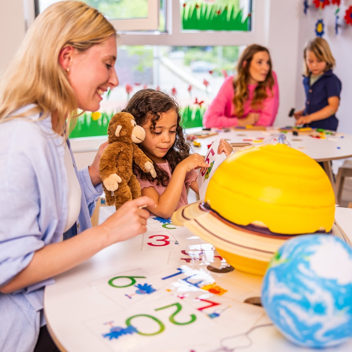Eine Erzieherin zeigt einem Vorschulkind verschiedene Planeten in der Kita kinderzimmer Hamburg